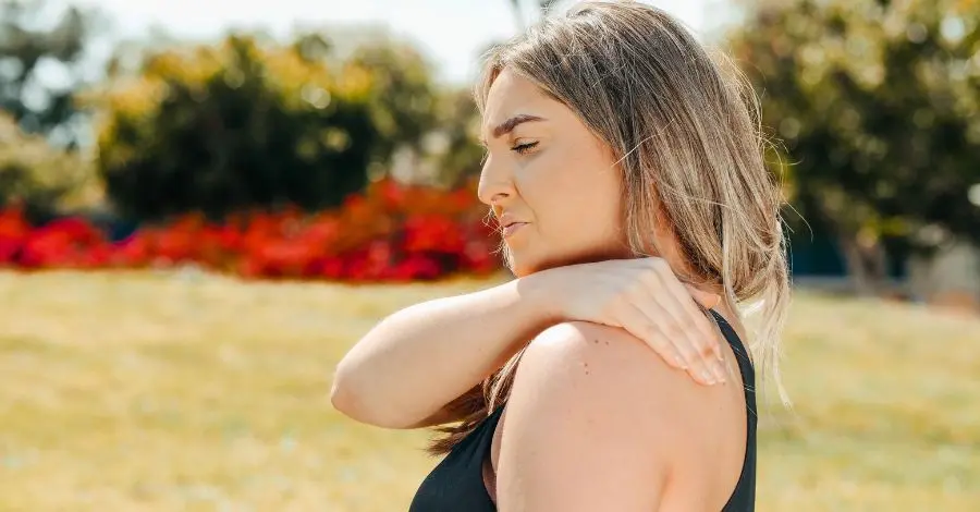 Mulher sentindo dor no ombro após treino, um exemplo de dor muscular tardia pós-treino.