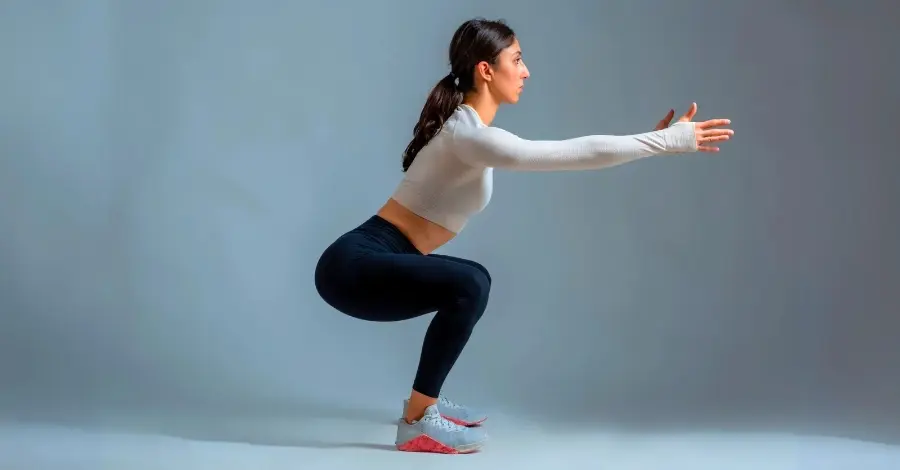 Mulher em posição de agachamento livre, demonstrando um exercício de peso corporal para fortalecer pernas e glúteos.