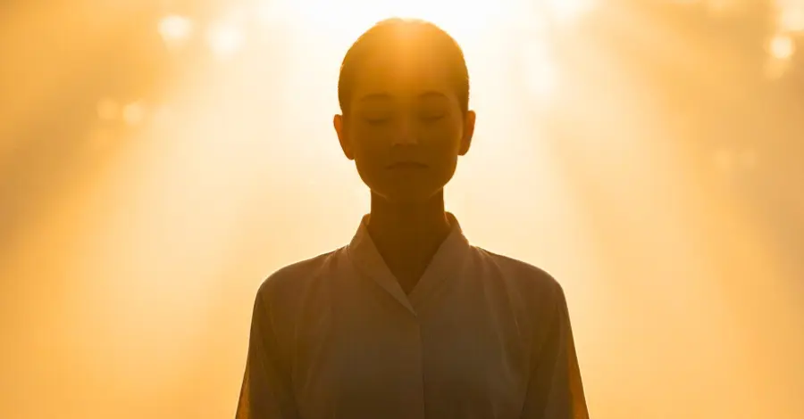 Mulher meditando sentada sob luz dourada, transmitindo calma e tranquilidade.