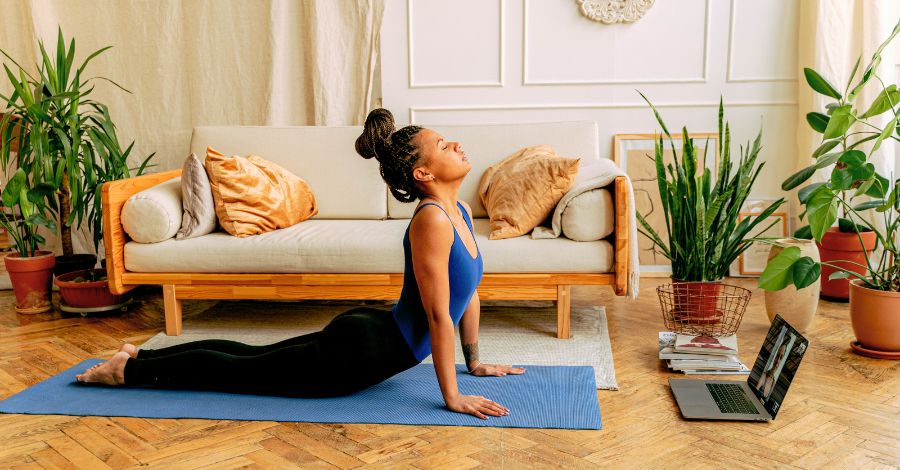 Mulher praticando yoga em casa com notebook aberto, seguindo uma aula online de yoga.